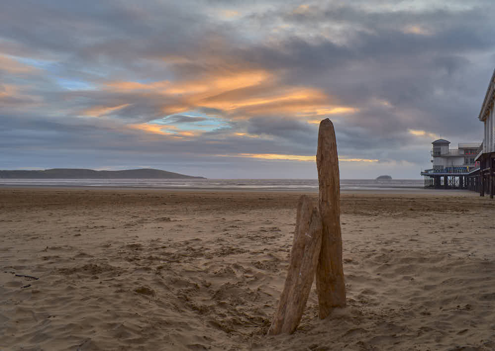 An image with low quality, showing the same image of driftwood on a beach, but with lower color intensity and object definition.